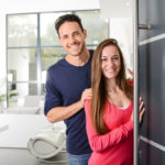 happy young couple at their new house front door welcoming people